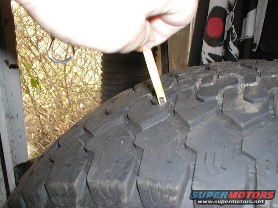 Hand holding a tape measure to check tread depth on a tire