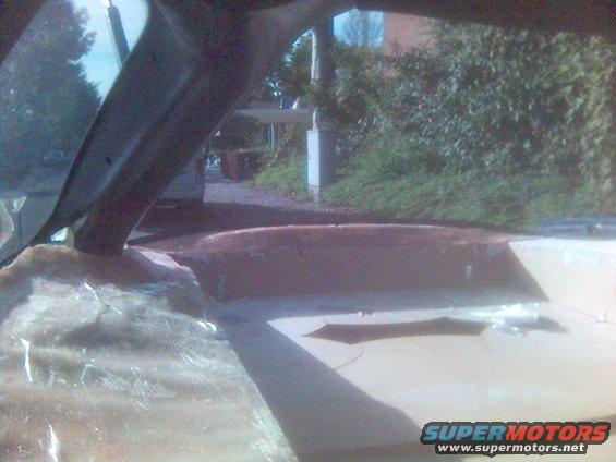 View from inside a car, looking over the dashboard at the windshield and outside scenery. The dashboard is partially covered