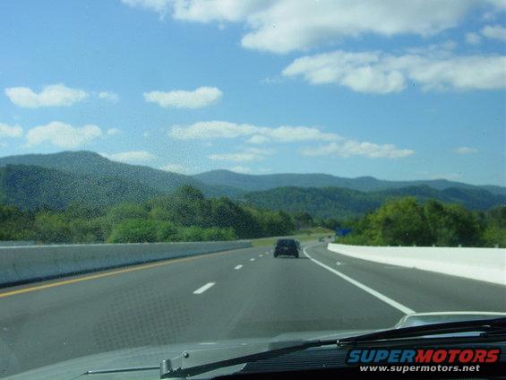 View from car on highway driving through mountains, another car ahead