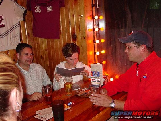 People gathered at a wooden table in a bar with jerseys on the wall
