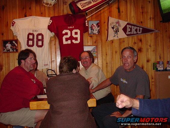 Four people sit at a table in a room decorated with football jerseys and pennants