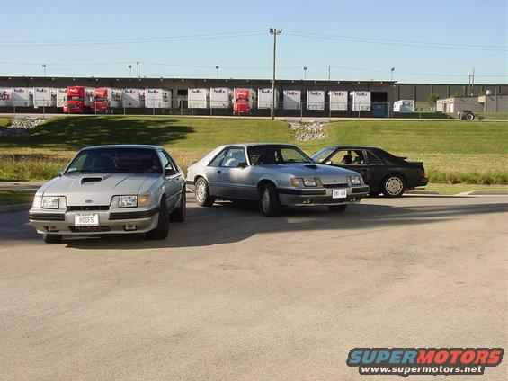 Three 1986 Ford Mustangs parked in front of a warehouse