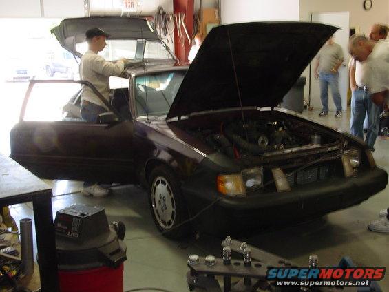 Dark red third-gen Ford Mustang with hood and doors open, people looking at engine