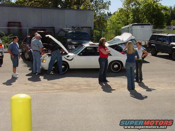 1986 Ford Mustang with hood open, people gathered around. Another SUV and car in background
