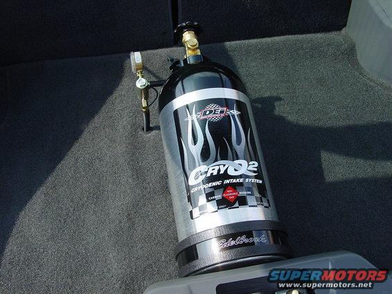 Nitrous oxide tank with Edelbrock base and "CRYQ2" graphics, mounted in a car's carpeted interior