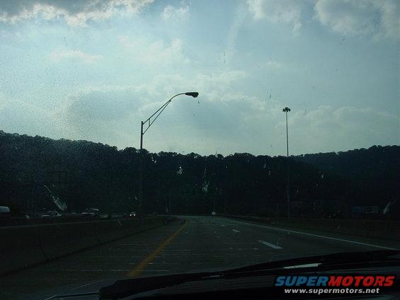 Highway driving scene with streetlights and trees under a cloudy sky