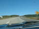 1978 Ford Mustang II - A view from inside a vehicle driving on a highway with trees and hills in the background.