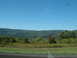 1978 Ford Mustang II - A wide view of rolling hills and trees under a clear blue sky, with a road in the foreground.