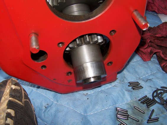 Red transmission housing with a gear and pins scattered on a blue cloth. A shoe is visible in the lower left