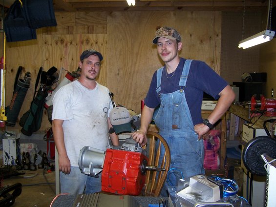 Two guys in a garage with a red transmission and a silver bell housing