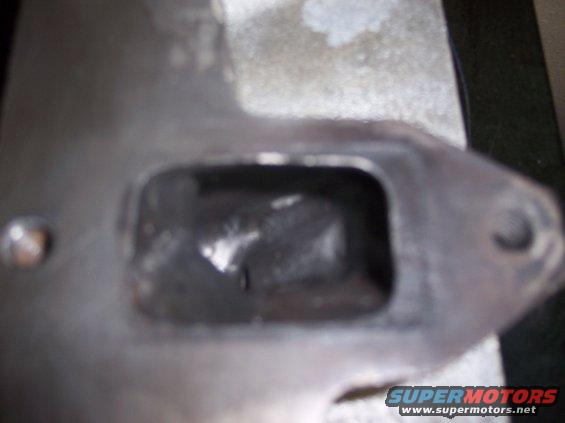 Close-up of a metal engine part with a rectangular opening and visible bolt holes