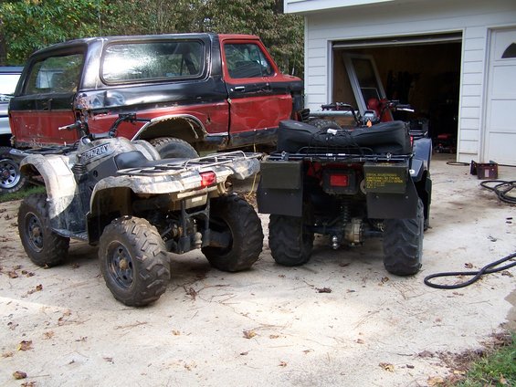 Rear view of two ATVs parked in front of a red and black Ford Bronco