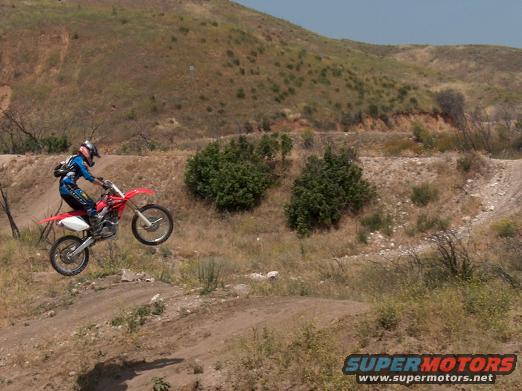 Red dirt bike airborne on a dirt track with a rider