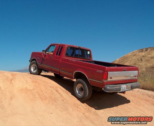 Red 1989 Ford F-250 pickup truck, rear 3/4 view, driving on dirt
