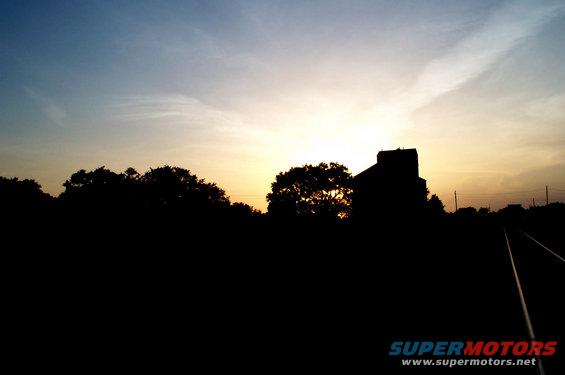 Sunset over railroad tracks with a silhouetted building and trees
