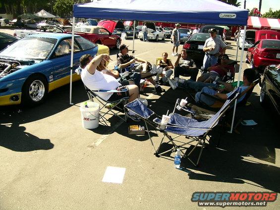 Blue and yellow 1993 Ford Probe with hood open, people sitting in chairs under a tent