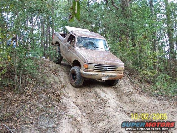 Muddy Ford pickup truck going up a dirt hill with trees around