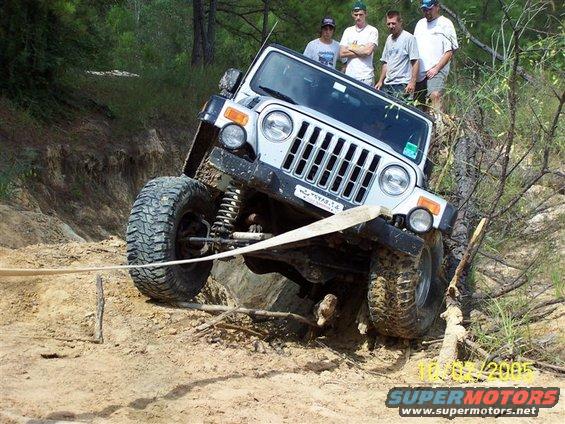 Silver Jeep Wrangler on a dirt trail, tilted on its side with a tow strap attached