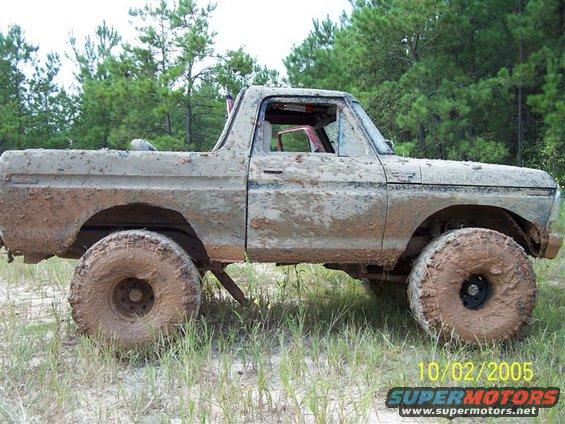 Muddy truck with big tires in a grassy, wooded area. Date stamp 10/02/2005 visible