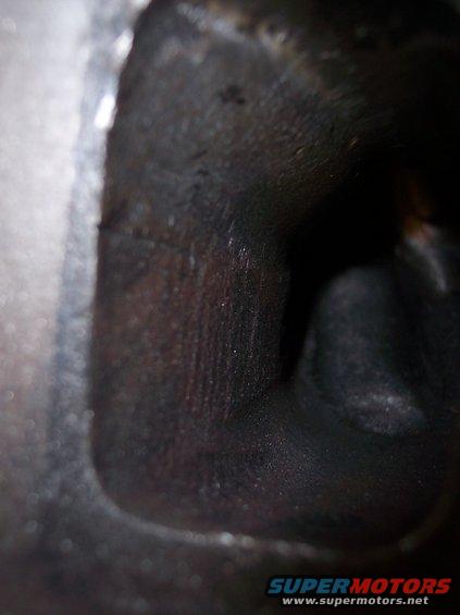 Close-up of a dark, internal engine component, possibly a cylinder head, showing machined surfaces and some carbon buildup