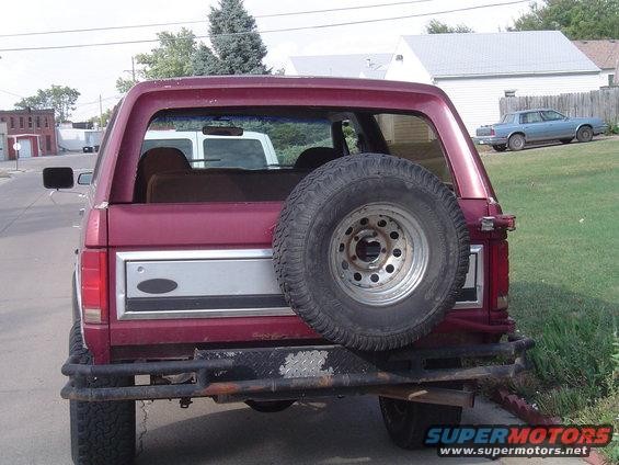 Maroon Ford Bronco rear view with spare tire mounted on the back. Aftermarket bumper visible