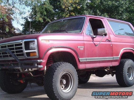 Red Ford Bronco with aftermarket bumper and large tires. Bronco badge visible on fender