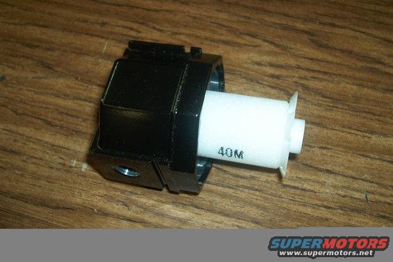 Black plastic automotive part with white cylindrical component labeled 40M on a wooden surface