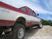 1979 Ford F-150 - A two-tone pickup truck is shown from a low angle, climbing a pile of gravel under a partly cloudy sky.
