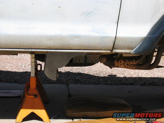 White vehicle undercarriage on jack stands, showing exhaust pipes and a metal shield