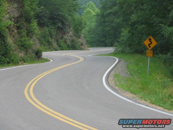 Winding mountain road with double yellow lines and a 20 MPH curve warning sign