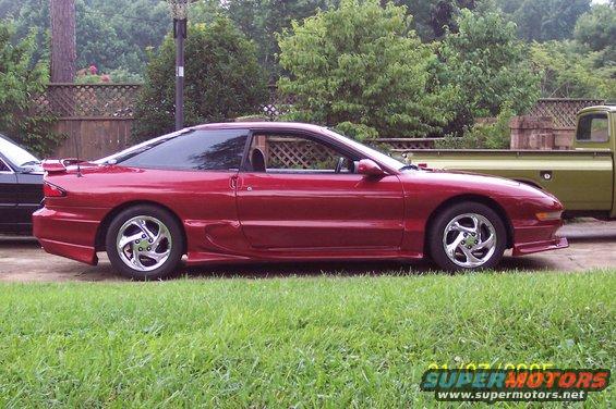 Red 1995 Ford Probe coupe with a spoiler and aftermarket wheels, seen from the side