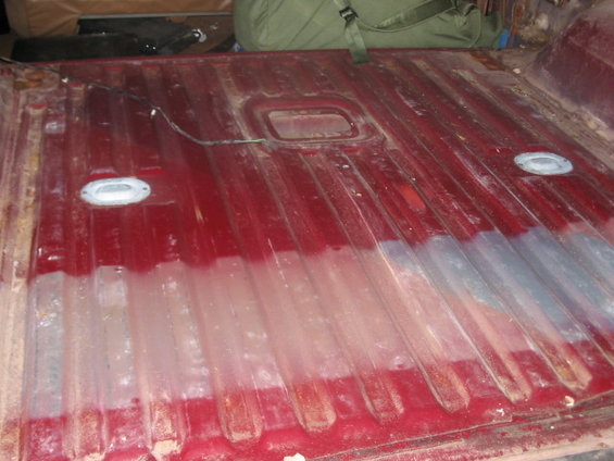 Red truck bed floor with ribbed metal, two tie-down points, and a central rectangular recess