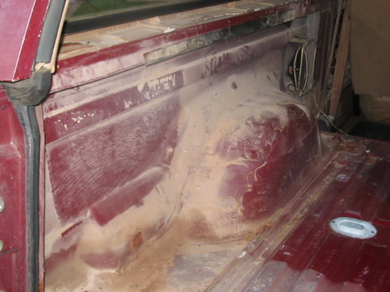 Interior cargo area of a vehicle, showing dusty red metal panels and some wiring