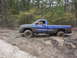 2005 Dodge 1500 - Muddy blue Dodge Ram pickup truck stuck in a wooded area. The vehicle is partially submerged in mud.