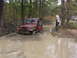 2005 Dodge 1500 - A red Jeep is stuck in the mud while two men stand nearby, with another vehicle in the background.