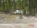 2005 Dodge 1500 - A white 2005 Dodge 1500 navigates a muddy trail in a wooded area, demonstrating its off-road capability.