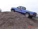 2005 Dodge 1500 - A blue pickup truck navigates an off-road obstacle, climbing a large pile of dirt.