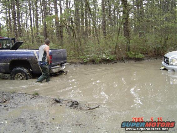 Blue pickup truck stuck in mud, with a silver truck visible in the background