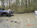 2005 Dodge 1500 - A person stands beside a blue pickup truck that is stuck in a muddy, water-filled area, with another vehicle partially visible in the dista…