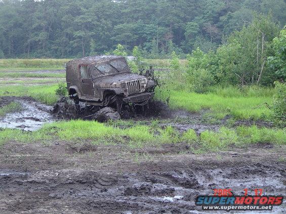 Mud-covered Jeep Wrangler TJ splashing through mud pit