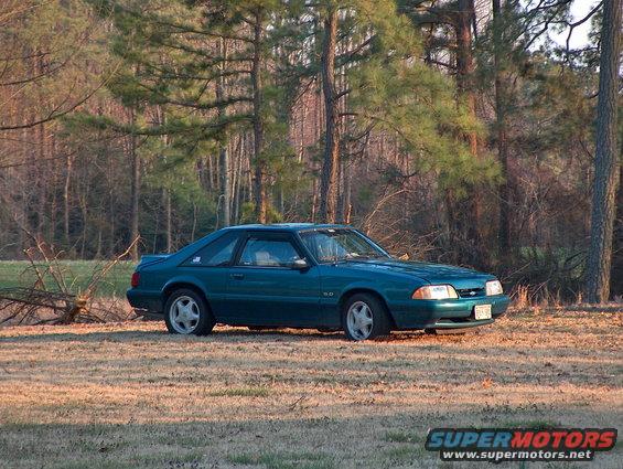 Teal 1993 Ford Mustang parked in a grassy field with trees in the background