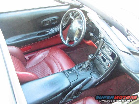 Interior shot of a car with red leather seats, black dashboard, and steering wheel. Center console has radio and gear shifter