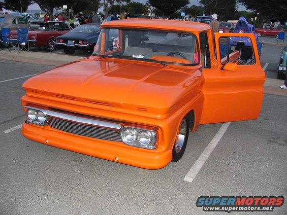 Orange pickup truck with driver's door open, chrome grille, and dual headlights