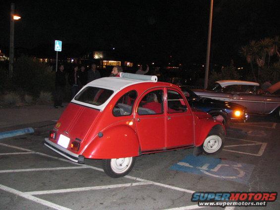 red Citroen 2CV parked in a lot at night, another car behind it