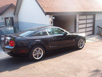 Black 2005 Ford Mustang coupe parked in driveway next to garage