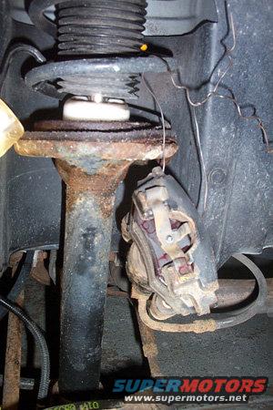 Close-up of a rusty car brake caliper and strut assembly with a coil spring