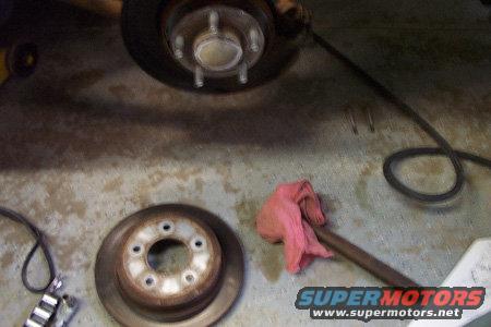 Car brake rotor and caliper assembly on concrete floor. A pink rag is on a tool