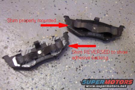 Disk brake pads with shims properly mounted and reversed to show adhesive backing