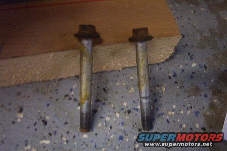 Two used bolts resting on a wooden plank over a speckled garage floor