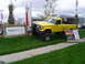 1985 Ford Bronco - A modified yellow pickup truck is parked outside a dealership with two signs in front of it.